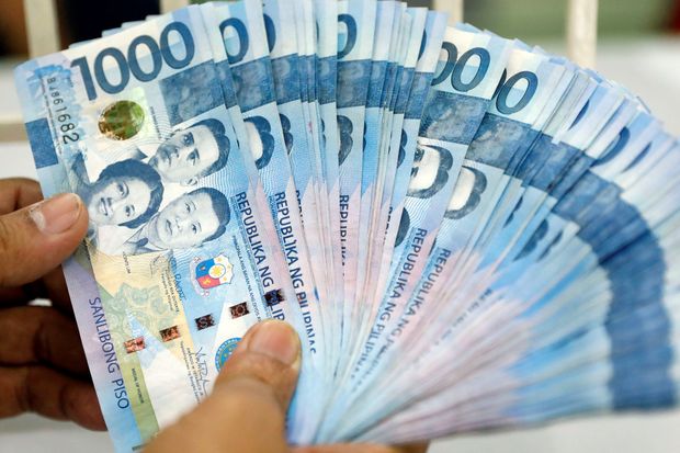 A worker shows Philippine peso bills inside a money changer in metro Manila